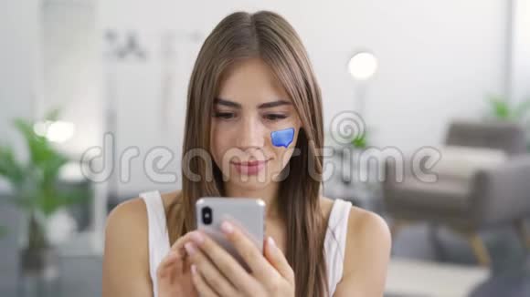 特写肖像年轻愉快的女人使用她的手机坐在家里女孩脸上画的留言框视频的预览图