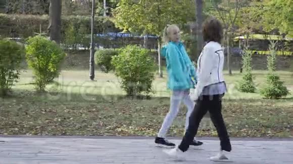 从侧面可以看到年轻的白种人祖母和她十几岁的孙女穿着休闲服装走在路上视频的预览图