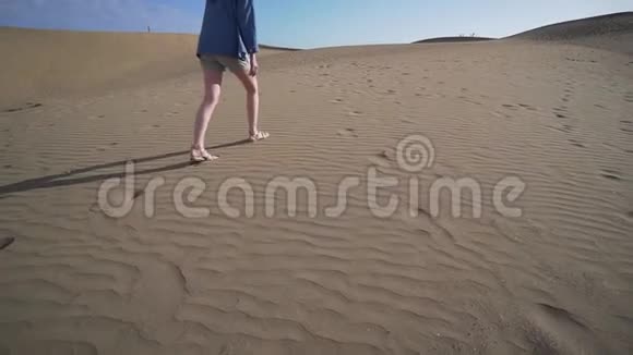沙漠景观女性腿在阳光明媚的日子里被风吹过的沙子背景下慢速移动广角视频的预览图