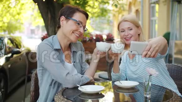 成熟的女士在露天咖啡屋拿着咖啡微笑着自拍视频的预览图