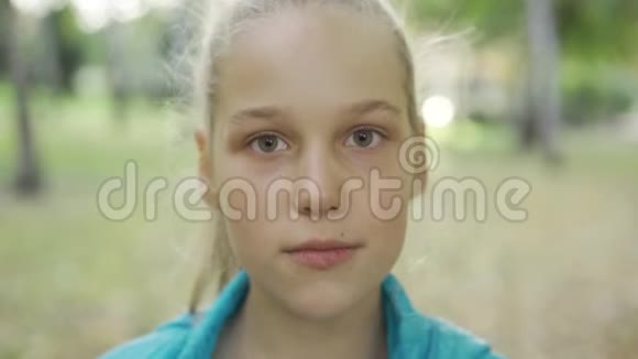 一个年轻愤怒的金发女孩看镜头的肖像美丽的白种人少年站在阳光明媚的公园里视频的预览图