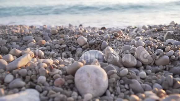 晚上拍摄一片石滩日落时的海岸太阳照耀下的海浪日出卵石海岸线4k视频的预览图