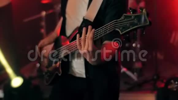 身着黑衬衫的年轻音乐家在充满红色的舞台上演奏黑色低音吉他视频的预览图