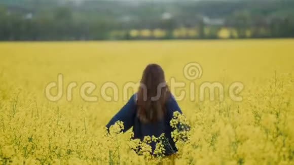 穿着蓝色毛衣的快乐女孩跑在黄色油菜花田里跳绳视频的预览图