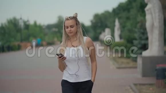 年轻的金发辫子女性走在街上听音乐视频的预览图
