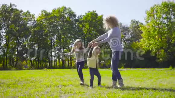 金发的白种人女人和两个漂亮的小女孩在草地上跳舞穿着休闲服的家庭视频的预览图