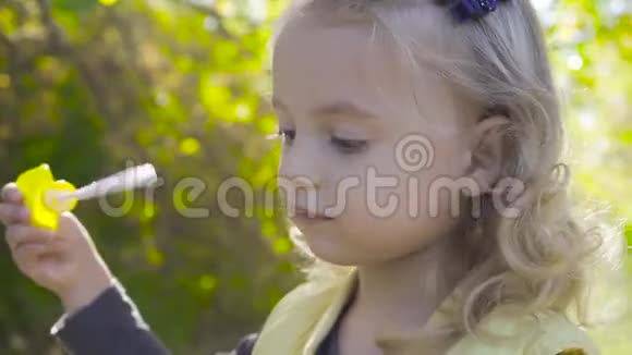侧面看到一个可爱的金发女孩吹着肥皂泡和微笑小可爱的孩子棕色的眼睛在玩视频的预览图