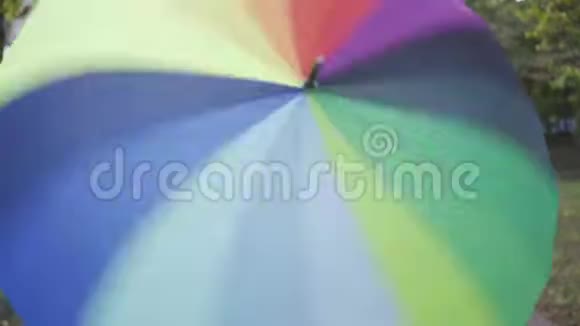 五颜六色的伞在前景上旋转年轻的微笑的女人出现在它的后面成年人视频的预览图
