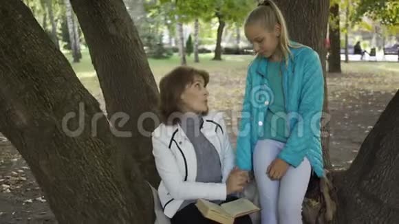 两位高加索妇女坐在秋天公园的树上讨论这本书的特写镜头漂亮的黑发女人视频的预览图