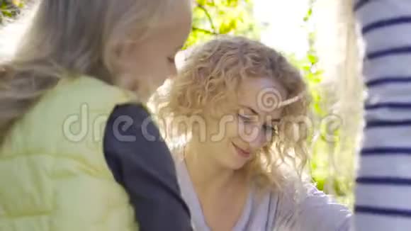 一位带着一头卷发的金发白种人微笑着坐在阳光下教她可爱的小女孩的肖像视频的预览图