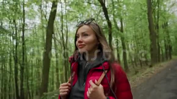 阳光明媚的春天美丽的女游客穿着红色夹克背着背包在茂密的森林里散步娱乐视频的预览图