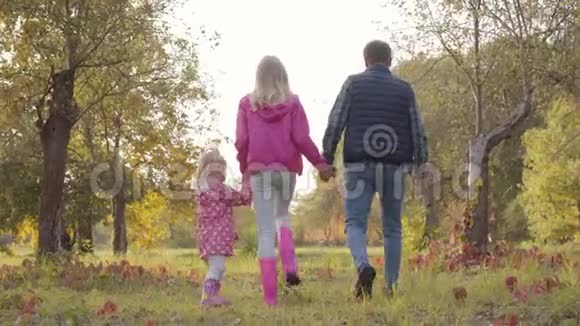 后景白种人男子漫步与他的两个女儿穿着粉红色的衣服在秋天公园幸福家庭视频的预览图