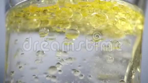 黄色的气泡漂浮在一个透明的水玻璃中特写黄色的油倒进一罐清澈的油中视频的预览图
