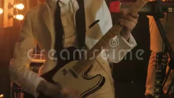 穿着白色西装和黑色领带的吉他手在舞台上用吉他弹奏和弦视频的预览图