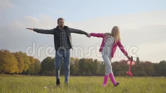 父女牵着手模仿苍蝇带着粉色玩具飞机的金发白种人女孩视频的预览图