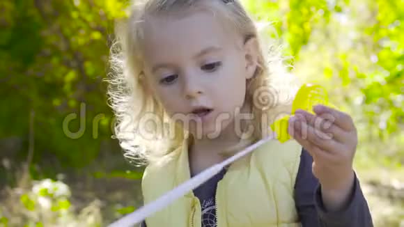 一个迷人的金发女孩留在阳光下吹肥皂泡的特写镜头一个棕色眼睛的小孩视频的预览图