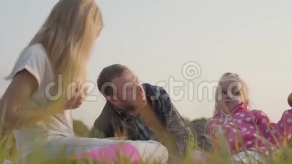年轻的白种人父亲和他的两个金发女儿在家庭野餐穿着休闲服装的幸福家庭视频的预览图