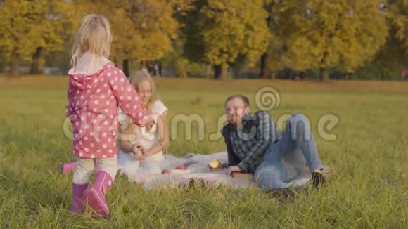 金发碧眼的小孩子穿着粉红色的衣服走到姐姐和父亲面前坐在秋天的草地上视频的预览图