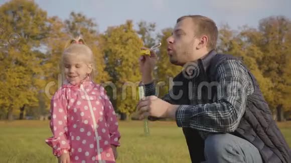 白人男子向他的小女儿展示如何吹肥皂泡父亲招待一个穿粉色衣服的可爱金发女孩视频的预览图