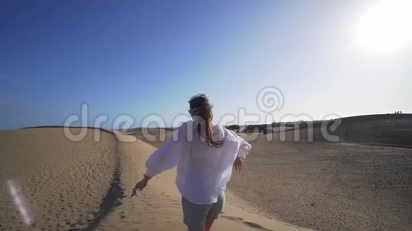 漂亮的年轻女子穿着白色衬衫戴着沙漠中的眼镜在沙丘上旋转着假期的乐趣视频的预览图