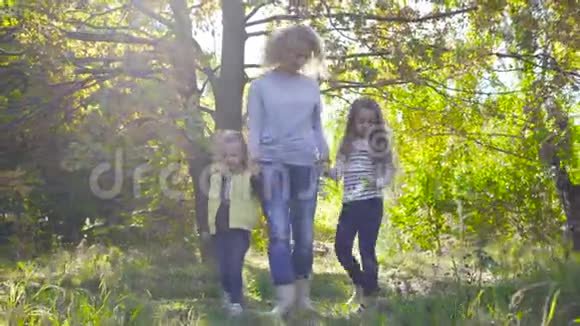 快乐的白种人一家人在秋天公园的阳光下漫步微笑着的成年卷发女子手牵着她的手视频的预览图