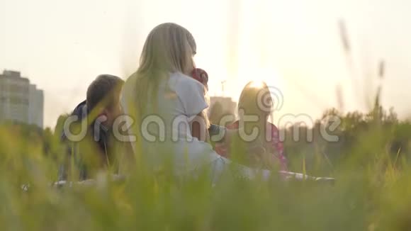 两个白种人女孩和他们的父亲坐在草地上晒太阳吃苹果快乐的家庭花时间视频的预览图
