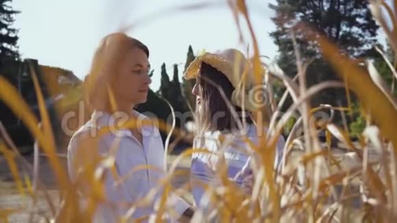 快乐的一对拥抱在黄草后面年轻英俊的男女戴着草帽在公园里共度时光视频的预览图