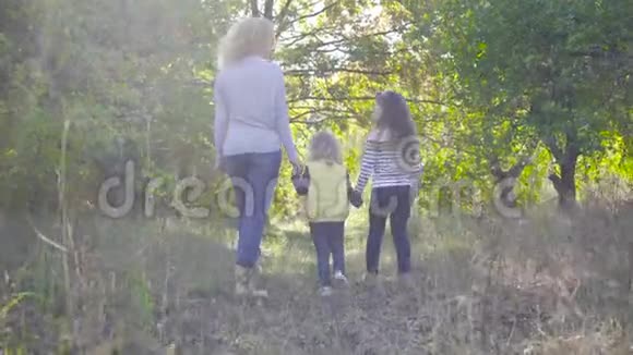 在秋天公园漫步的一个幸福的高加索家庭的后景微笑着的成年卷发女子手牵着她的手视频的预览图