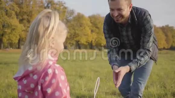 微笑的白种人胡须男教他的小女儿玩肥皂泡可爱的金发女孩穿着点缀的粉红色视频的预览图
