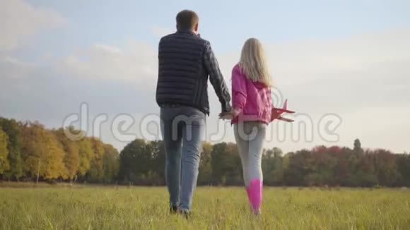 一个年轻的金发白种人女孩抱着粉红色的玩具飞机旋转着父亲和他的孩子一起散步视频的预览图