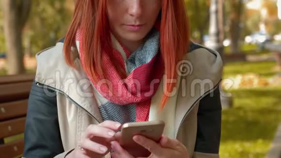 在阳光明媚的天气里长着狐毛的女孩坐在长凳上使用智能手机并在网上订购视频的预览图
