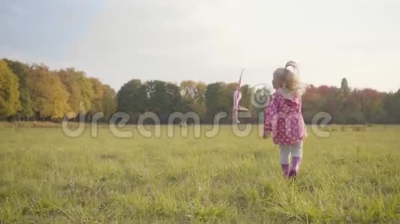 穿着点缀的粉红色夹克和橡胶靴的金发白种人小女孩在户外玩玩具飞机可爱视频的预览图