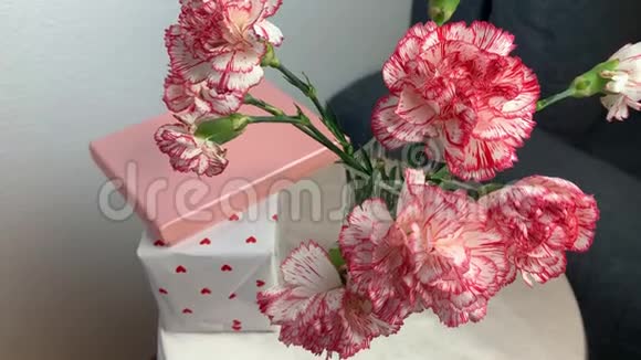 一束粉红色的康乃馨花放在花瓶里盒子里的礼物放在一张灰色沙发旁边的圆桌上甜蜜的概念视频的预览图