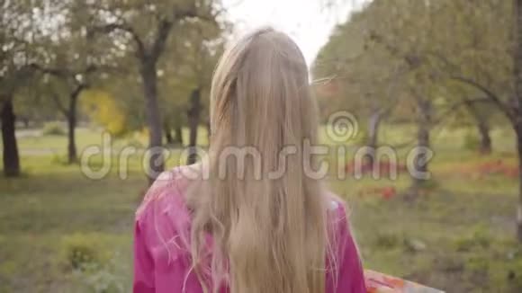 金发白种人少年在秋天的森林里漫步的特写镜头穿着粉红色衣服的开朗的少女视频的预览图