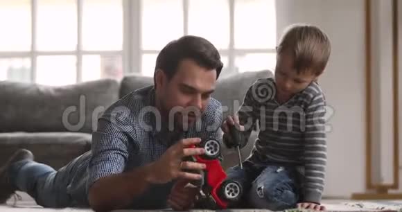爸爸教可爱的孩子玩玩具车在地板上视频的预览图