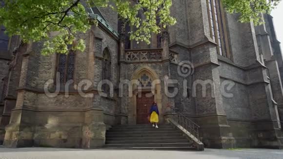 穿着毛衣和黄色裙子的开朗女孩沿着教堂的台阶跑下来开始在阳光下旋转视频的预览图