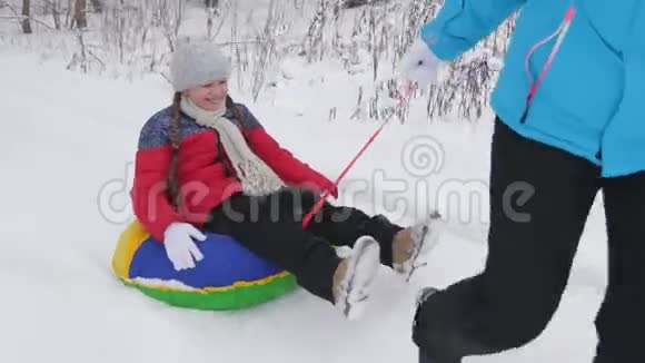 妈妈带着一个快乐的女儿在一条白色和雪的路上雪橇上孩子骑着一根管子里面装满了视频的预览图