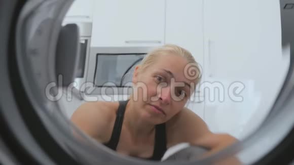 一个女人坐在洗衣机前面打开门看着里面的鼓视频的预览图
