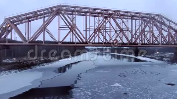 低空飞越冰冻河流的铁路桥下飞行无人机的鸟瞰图视频的预览图