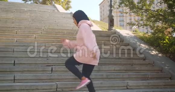 年轻迷人的非洲裔美国穆斯林女孩在头巾上慢跑上下楼在城市玩的特写镜头视频的预览图