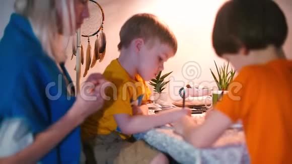 一位年轻的母亲和两个孩子在桌子旁做学校作业视频的预览图