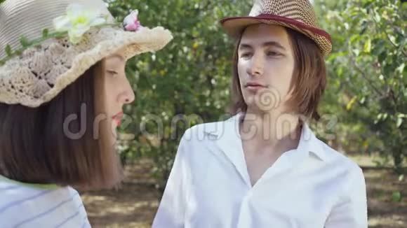 可爱的一对戴着帽子的夫妇站在公园里留着长发的男人抚摸着戴着帽子的漂亮女人的头发情人支出视频的预览图