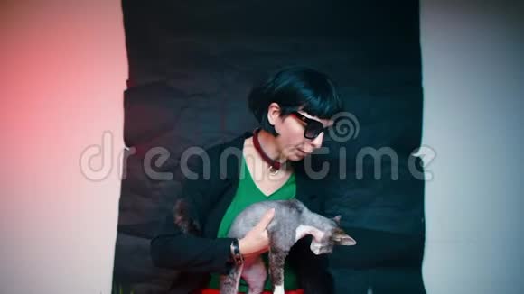 一个穿着深色衣服的女人抚摸着一只德文克斯猫在她怀里视频的预览图
