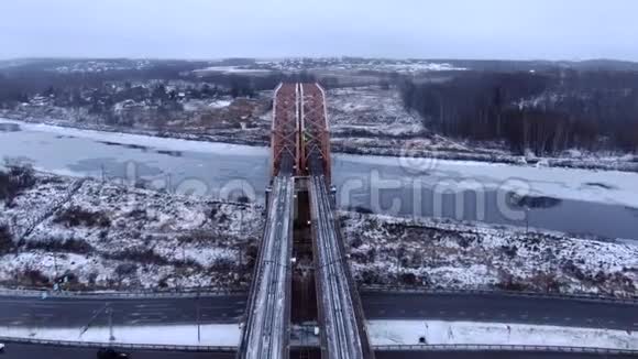 低空飞越冰冻河流的铁路桥上的无人机的鸟瞰图视频的预览图