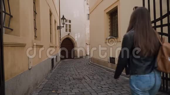 穿着牛仔裤和背包的女孩正沿着美丽狭窄的老街散步墙上有路灯拱门视频的预览图