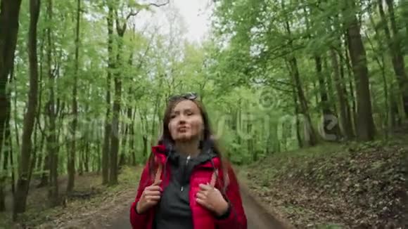 沿着森林道路积极健康的女性徒步旅行穿红色夹克和太阳镜的美女游客画像视频的预览图