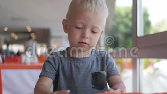 可爱的小男孩坐在街头咖啡馆看着电话坐在咖啡馆里用电话看动画片的漂亮孩子视频的预览图