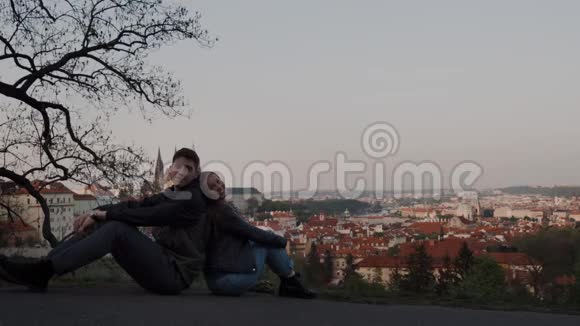 相爱的一对夫妇背靠背坐在观景台上可以看到布拉格的全景他们愉快地看着摄像机展示视频的预览图