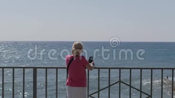 一位女士站在海边用智能手机拍摄风暴和海浪视频的预览图