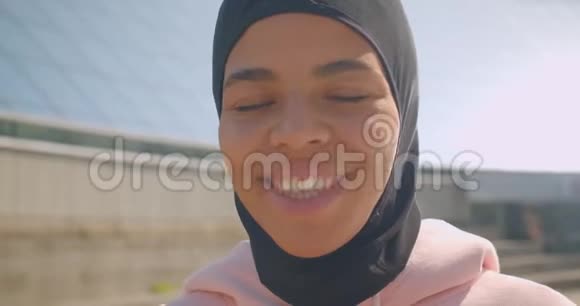 年轻漂亮的非洲裔美国穆斯林女孩戴着头巾看着镜头开心地在体育场微笑视频的预览图